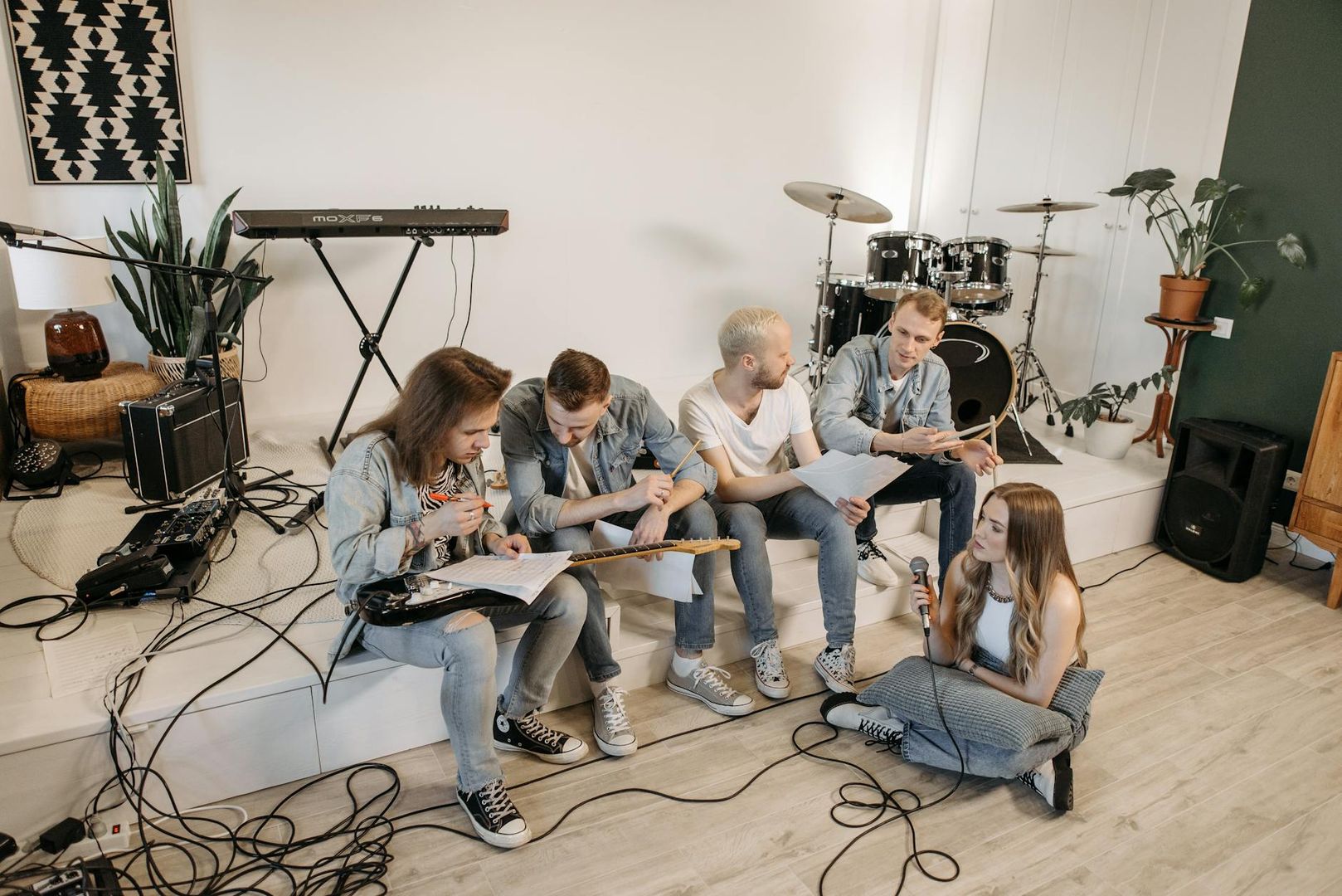 Eine Musikband probt: Fünf junge Leute in Jeans sitzen mit Instrumenten und Noten zusammen.